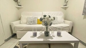 En hvid sofa med dekorative puder og en vase med blomster på et hvidt bord.