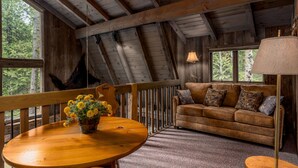 L’intérieur d’un chalet rustique, avec une table à manger en bois, un canapé agrémenté de coussins à motifs et un luminaire suspendu.
