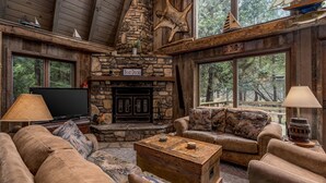 L’intérieur chaleureux d’un chalet avec une cheminée en pierre, des meubles en bois et de grandes fenêtres donnant sur la forêt.