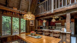 L’intérieur d’un chalet rustique est aménagé avec une table à manger en bois, des bancs et un coin cuisine doté de meubles en bois et d’un réfrigérateur.