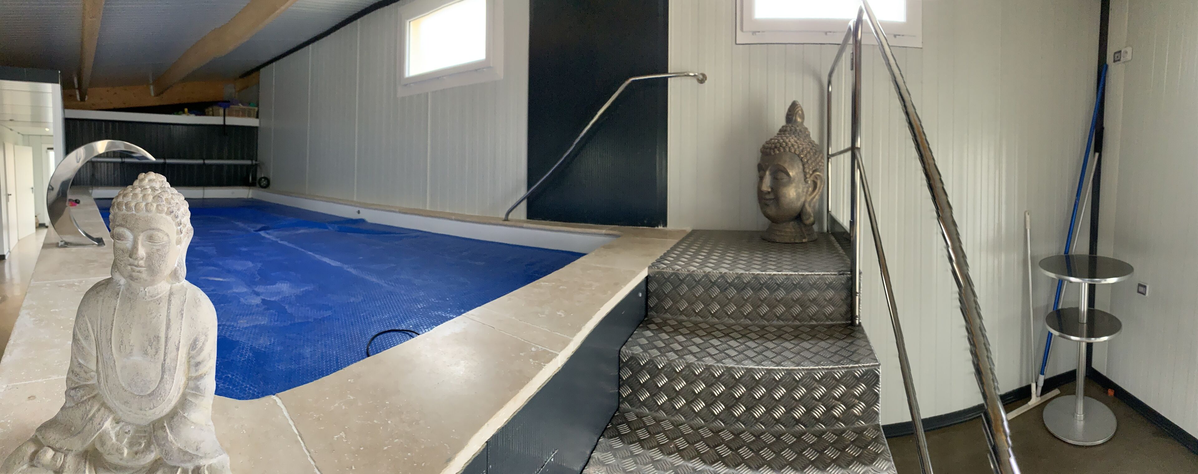 En swimmingpool med en Buddha-staty, en metallstege och en Buddha-staty placerad på en trappa.