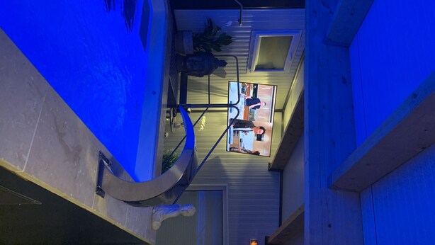 Un bâtiment moderne dont l’intérieur est illuminé de lumière bleue, avec un escalier et une statue.