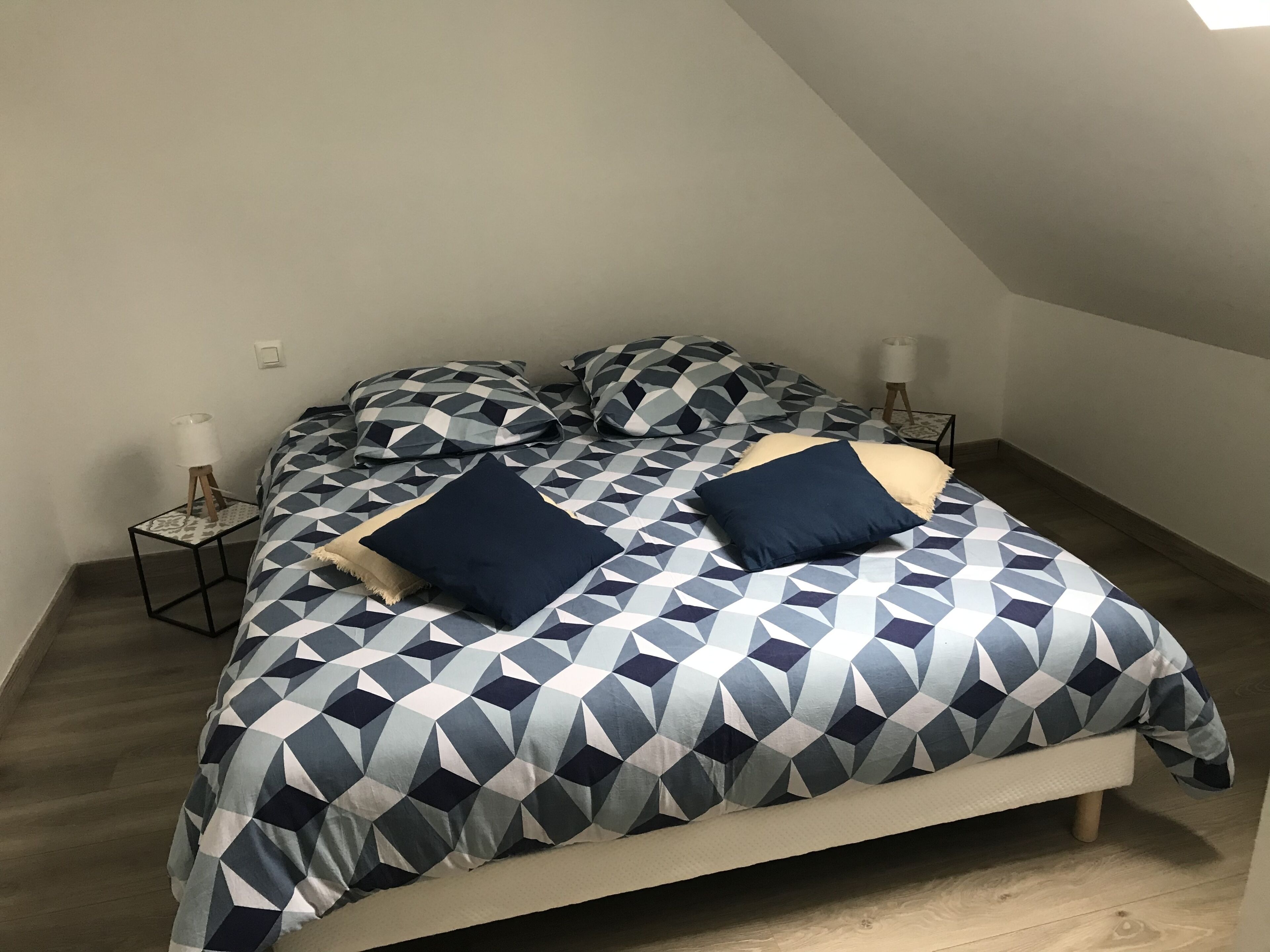 Ett sovrum med en säng, sängkläder med geometriskt mönster, två sänglampor och ett litet bord med en lampa.