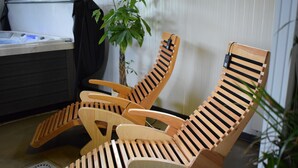 Trois fauteuils en bois, dotés d’un dossier et d’accoudoirs à lattes, sont disposés dans une pièce où se trouvent une petite plante et un mur blanc.
