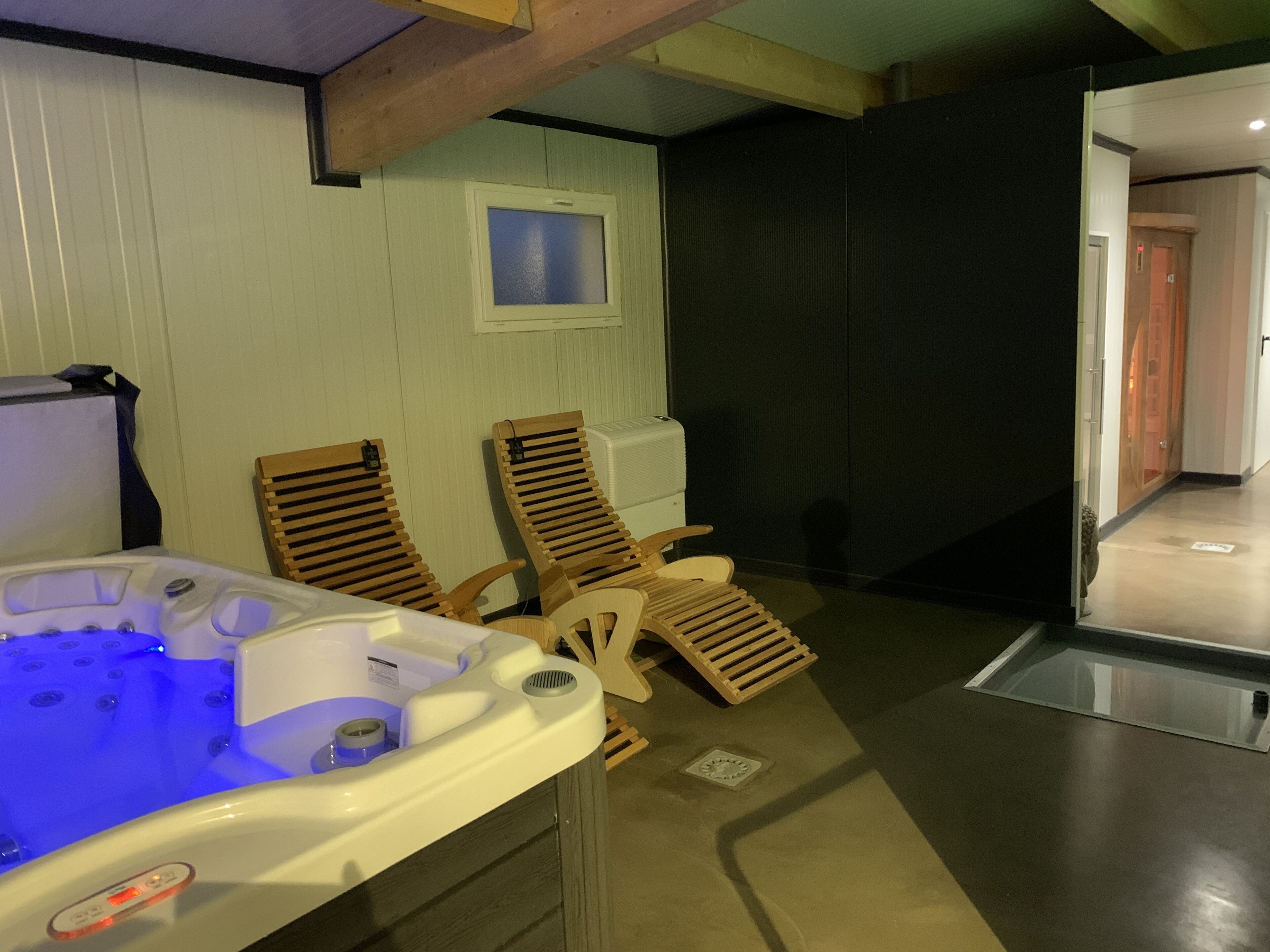 Habitación de spa con un jacuzzi, dos sillones de madera, un ventanal y una puerta que conduce a otra zona.