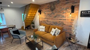 Un salon moderne avec un canapé marron, deux fauteuils, une table basse et un escalier menant à un niveau supérieur.