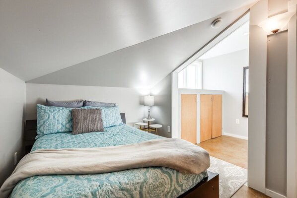 Een slaapkamer met een bed, nachtkastje, lamp en een kledingkast.