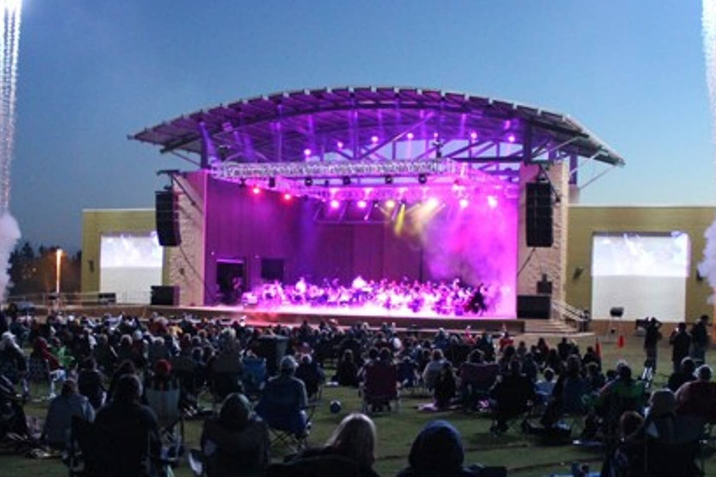 A large outdoor stage with a covered performance area and a crowd of people seated in front.