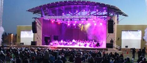A large outdoor stage with a covered performance area and a crowd of people seated in front.