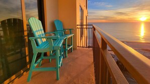 Een balkon met twee turquoise Adirondack-stoelen en een tafel, met uitzicht op een zonsondergang boven de oceaan.