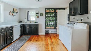 A modern kitchen with dark cabinets, a dishwasher, a washing machine, and a built-in plant wall. - Cozy Farmhouse by Shenandoah with Mountain Views (2, East Luray)