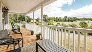 A covered porch with wooden flooring, white railings, and a view of a green landscape. - Cozy Farmhouse by Shenandoah with Mountain Views (2, East Luray)