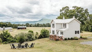 A white house with a porch and a table with chairs in a grassy area. - Cozy Farmhouse by Shenandoah with Mountain Views (2, East Luray)