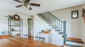 A dining area with a wooden table and chairs, a ceiling fan, and a staircase with a blue railing. - Cozy Farmhouse by Shenandoah with Mountain Views (2, East Luray)