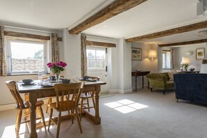 Comedor con una mesa de madera dispuesta para cuatro personas, un jarrón con flores y vistas al exterior a través de grandes ventanales.