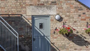 Una porta grigia con una piccola finestra, un cancello in metallo e un muro di mattoni con un cesto di fiori appeso.