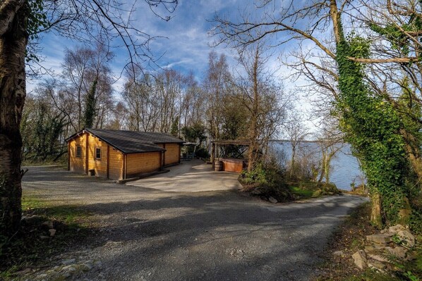 A rustic cabin with a gravel driveway leading to a wooden dock over water. - Log Cabin on the Lake - Sleeps 4 & Jacuzzi (Garrykennedy)