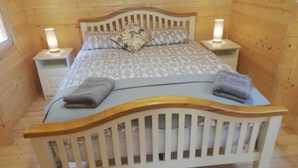 A cozy wooden room with a bed, two bedside tables, and a nightstand.