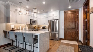 Una cocina moderna con armarios blancos, electrodomésticos de acero inoxidable y una isla central con taburetes de bar.