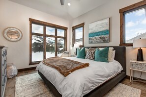 Quarto com uma cama grande, duas janelas, um quadro e uma mesa de cabeceira.