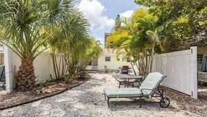 Un patio con mobiliario, palmeras y una valla blanca.