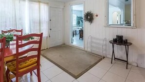 Habitación con una mesa de comedor, sillas, ventilador de techo, una mesita con una tetera y una puerta que da a otra habitación.