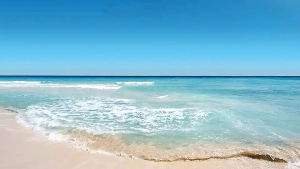 Una playa con agua azul cristalina y una orilla arenosa.