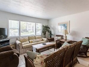 Relax in this inviting living room with a sofa, coffee table, and TV, surrounded by natural light and a potted plant.