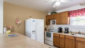 Una cocina con armarios de madera, un refrigerador blanco, una estufa y un ventilador de techo.
