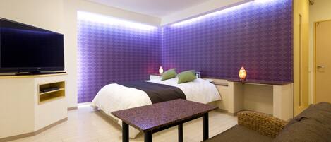 A modern hotel room with a bed, a flat-screen TV, a small table, and a sofa.