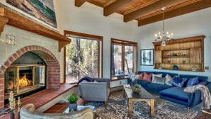 A spacious living room with a fireplace, large windows, a blue sofa, and a wooden ceiling.