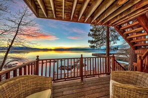 A wooden deck with wicker chairs overlooking a calm lake at sunset.