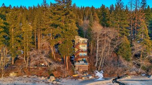 A multi-story building with a balcony, surrounded by dense forest and a frozen river.