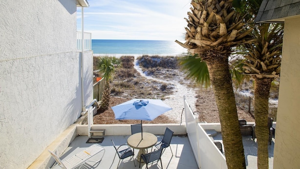 Un balcón con vistas a la playa, una mesa con sillas y una sombrilla azul.