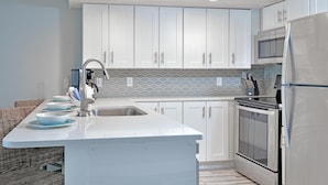 Una cocina moderna con armarios blancos, un refrigerador de acero inoxidable, un horno empotrado y un microondas.