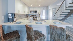 Una cocina moderna con armarios blancos, electrodomésticos de acero inoxidable y una isla central con taburetes de bar.