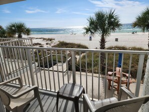 A balcony with a view of the beach, including a wooden deck, chairs, and a table. - Ambassador 122 - Gulf Front - Pet Friendly (Panama City Beach)