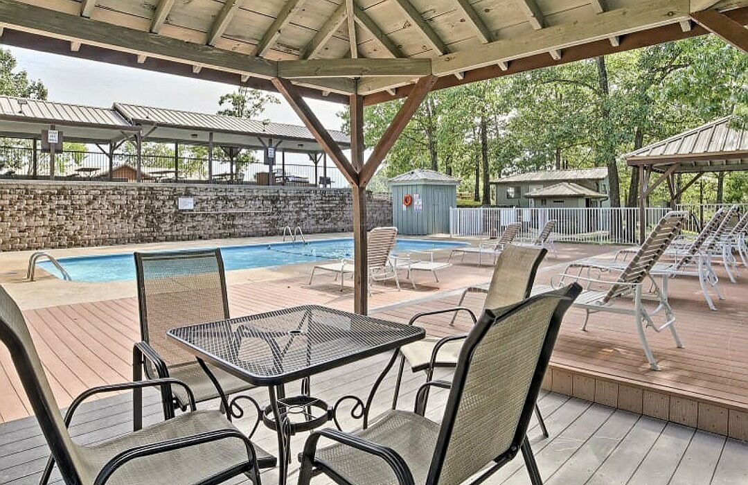 Un espace piscine extérieur abrité, doté de chaises longues et d’une table, entouré d’un mur de pierre et d’arbres.