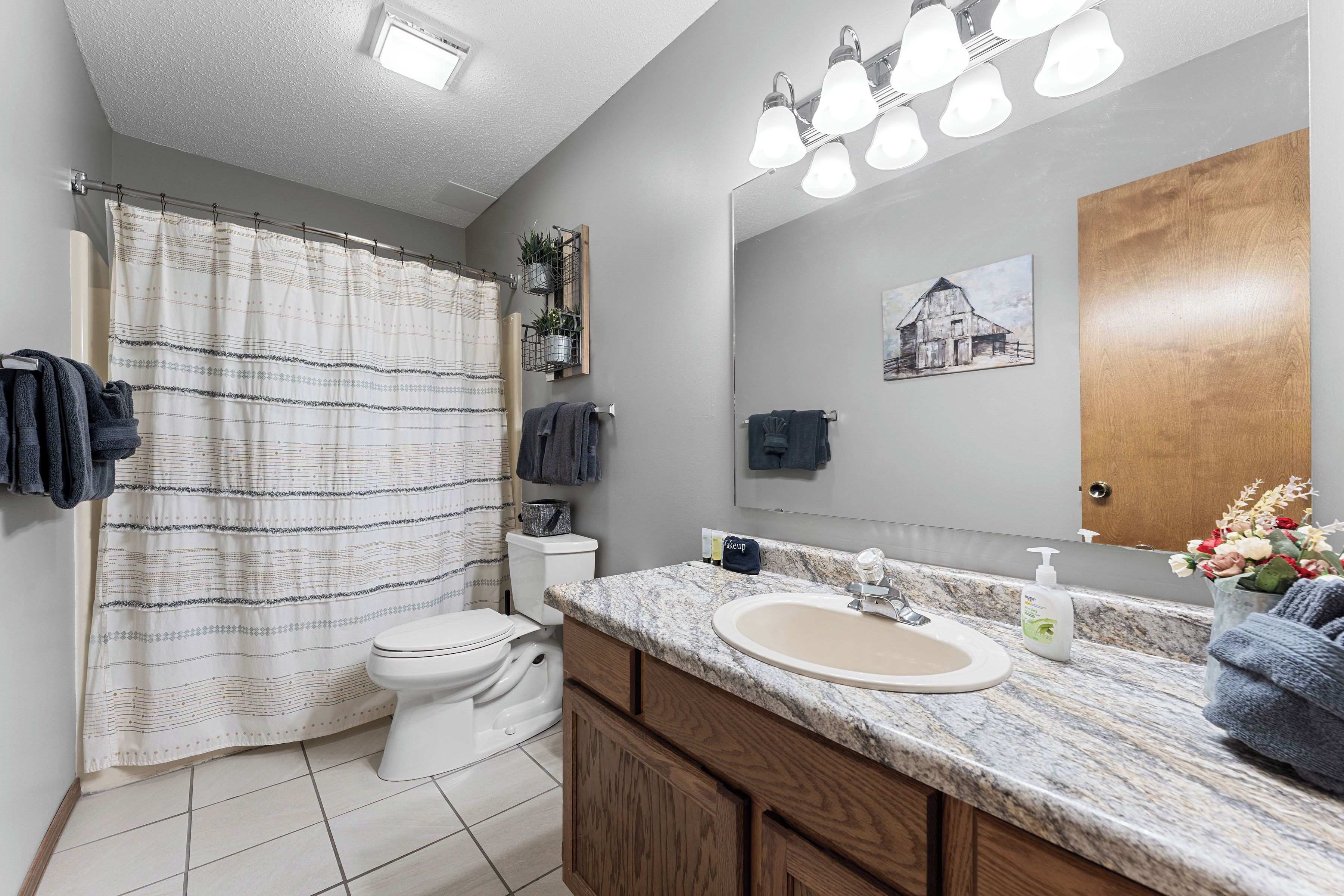 A modern bathroom with a shower curtain, toilet, sink, and wooden cabinets.