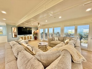 Ein geräumiges Wohnzimmer mit einer großen Eckcouch, einem Flachbildfernseher und einem Balkon mit Blick.