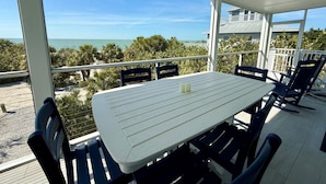 Ein überdachter Außenbereich mit Tisch und Stühlen, mit Blick auf Strand und Meer.