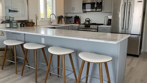 Eine moderne Küche mit einer großen Kochinsel, Barhocker, Edelstahlgeräten und Blick ins Freie.