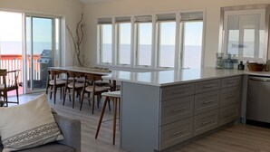 Moderni keittiö, jossa on suuri keittiösaareke, ruokailutila ja näkymä merelle.