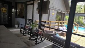 A covered outdoor seating area with chairs and a table, a pool in the background, and a staircase leading to the upper level.
