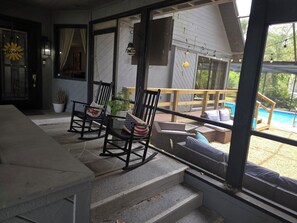 A covered outdoor seating area with chairs and a table, a pool in the background, and a staircase leading to the upper level.