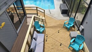 A poolside area with a wooden deck, blue chairs, a sofa, and a TV.