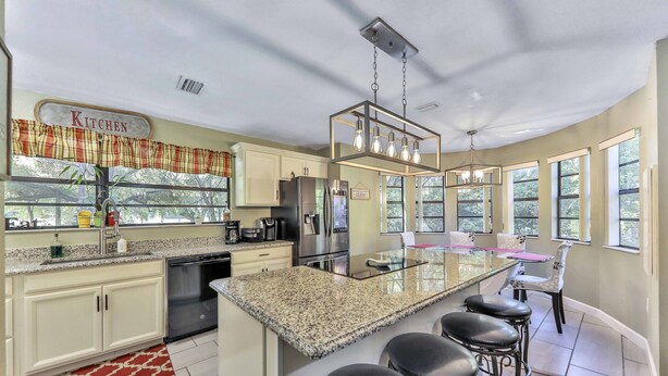 A modern kitchen with a granite countertop, stainless steel appliances, and a bar area with stools.