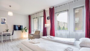 Ein modernes Hotelzimmer mit einem großen Bett, einem Schreibtisch mit Stuhl, einem Fernseher und einem Fenster mit roten Vorhängen.