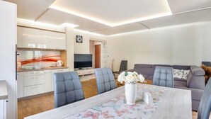 Una sala de estar moderna con una mesa de comedor, sofás grises y un televisor al fondo.