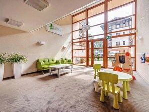 Ein Kinderspielbereich mit einer grünen Couch, einem weißen Tisch und gelben Stühlen.